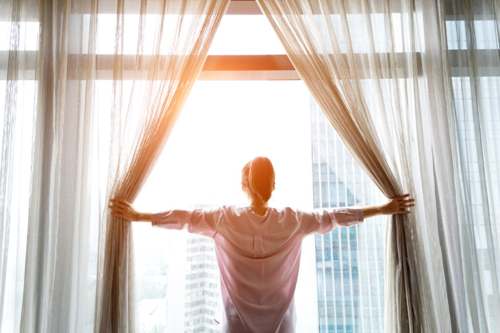 Woman opening curtains to start her morning routine