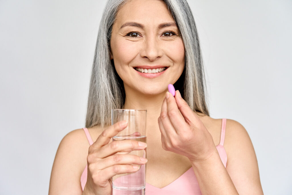 Portrait of happy smiling mid aged Asian woman taking pills isolated on white.