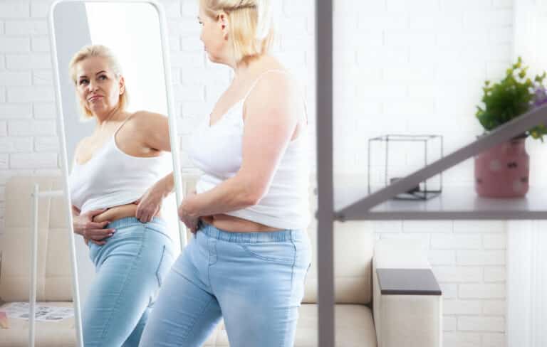 Woman looking at self in mirror; weight loss; stomach or belly fat