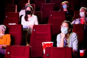 Young woman and the other spectators wearing protective face masks at the cinema