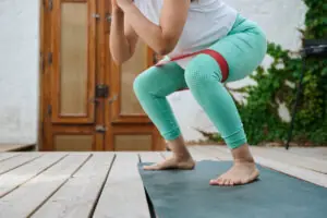 Woman exercising squat with resistance band on yoga mat outdoors for strength training and fitness. Benefits of Banded Squats
