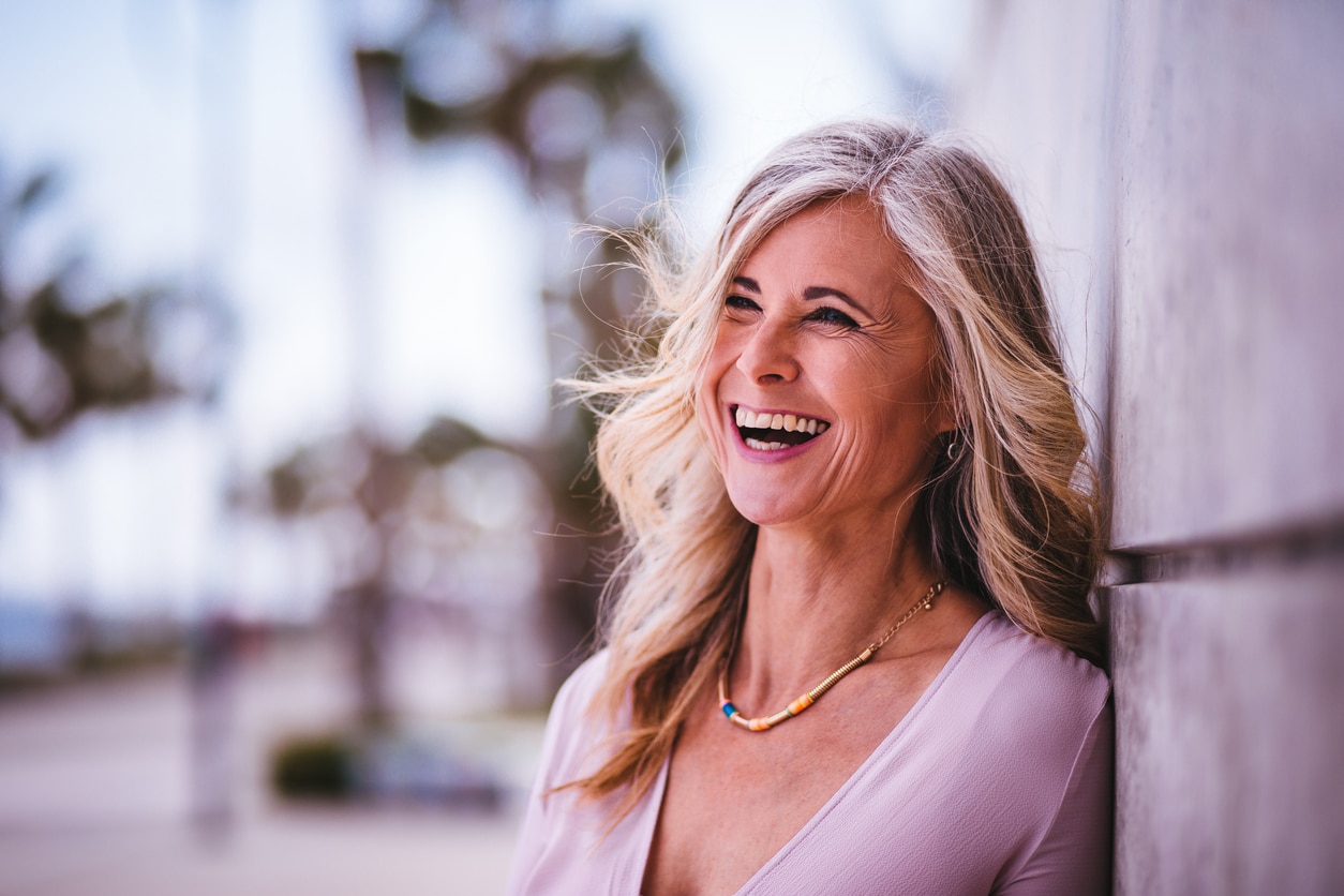 Beautiful stylish senior woman laughing leaning against wall outdoors