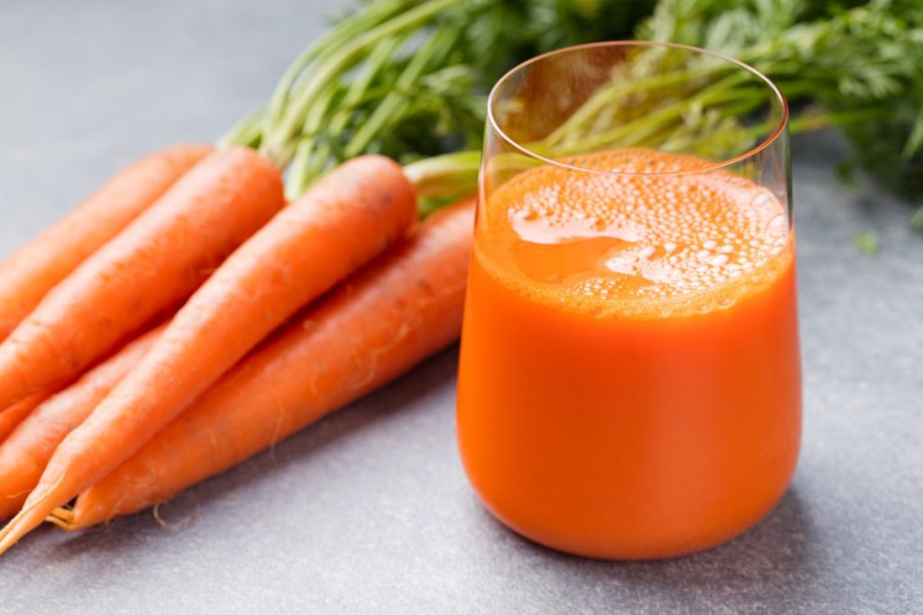 Carrot juice in a glass and fresh carrots beside it
