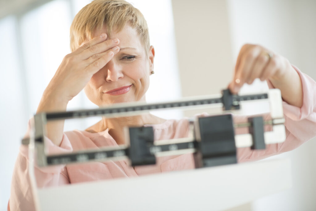 Postmenopausal woman on scale, frustrated because she's unable to lose weight