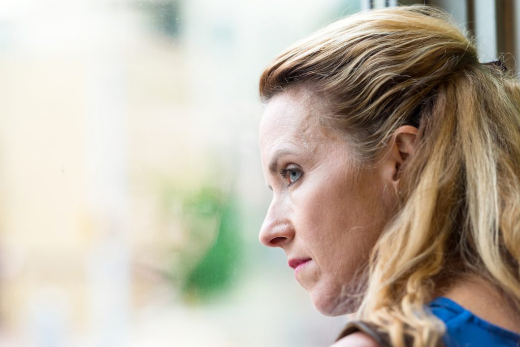 Depressed woman looking out window to show Keratin can be used as a treatment for depression