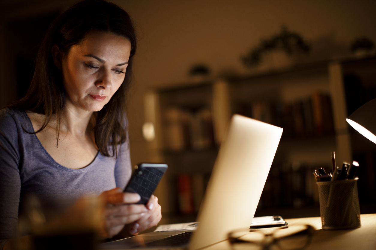 Woman working at computer and looking down at phone causes text neck