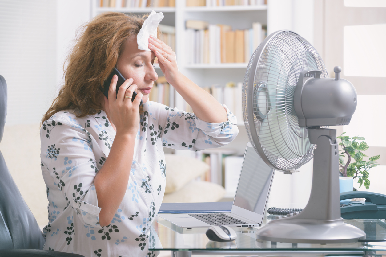 Woman having a hot flash sitting in front of a fan for relief