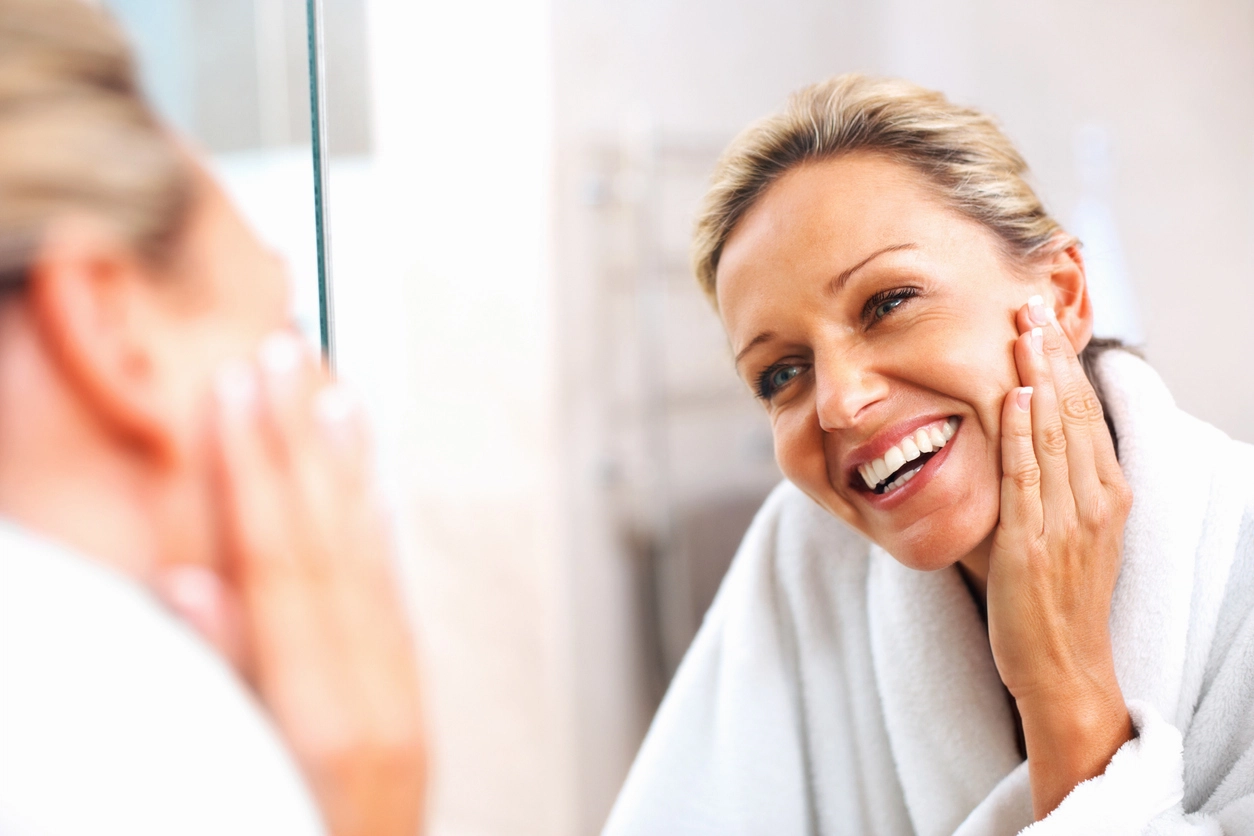Woman looking at her face in the mirror smiling