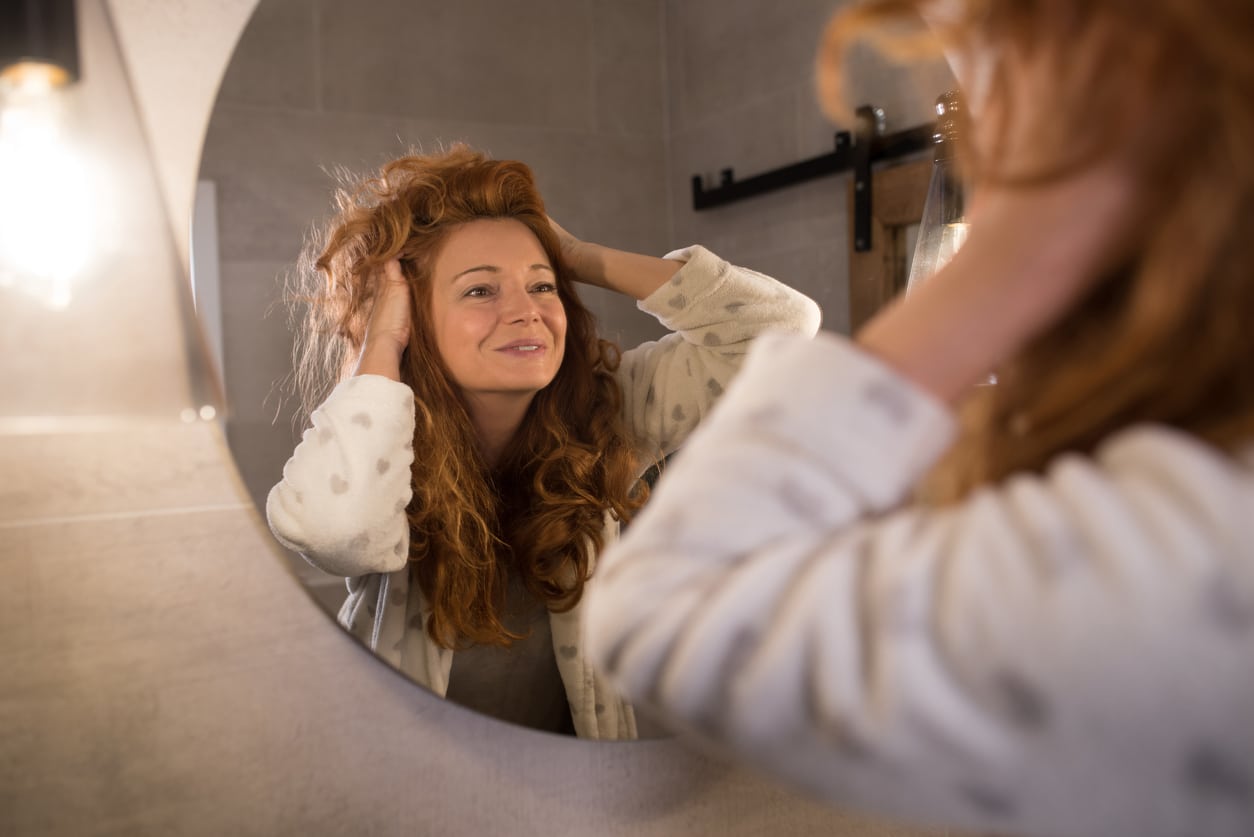Woman with thick hair smiling at self in mirror