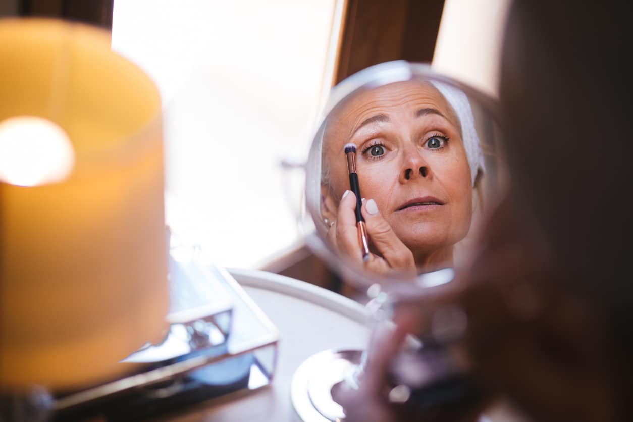 Woman doing her eye makeup in a magnified mirror