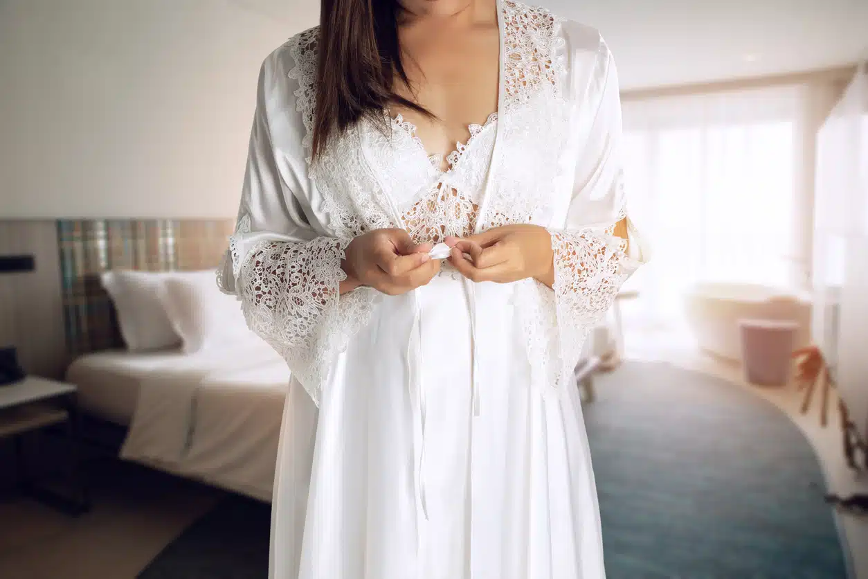 Women wearing white nightgown and long sleeve satin robe with floral lace in the bedroom, A girl trying on new white nightwear for sleep.