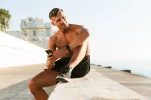 Photo of strong mature sportsman chatting by mobile phone on the beach outdoors.