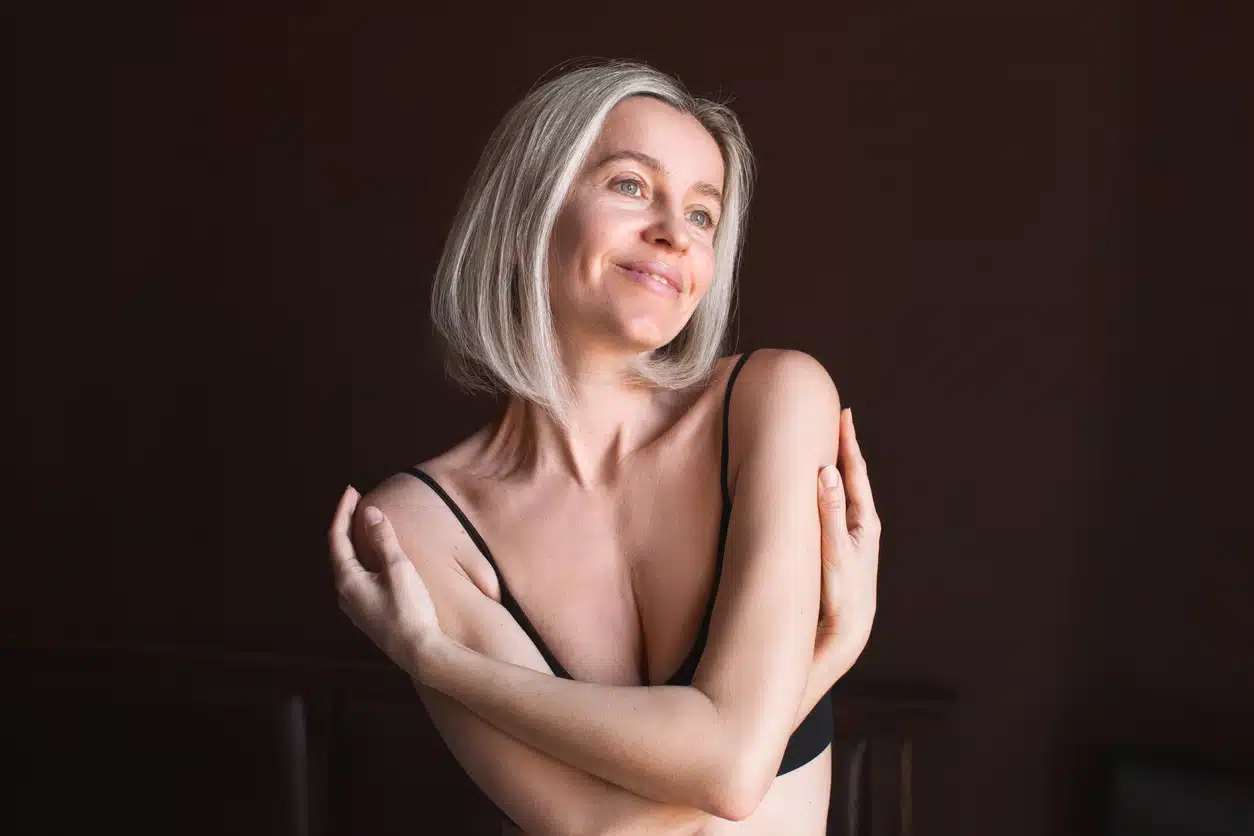 Attractive middle-aged woman enjoys herself and her body, loves herself. 40-year-old female hugs herself in the bedroom at home in the morning