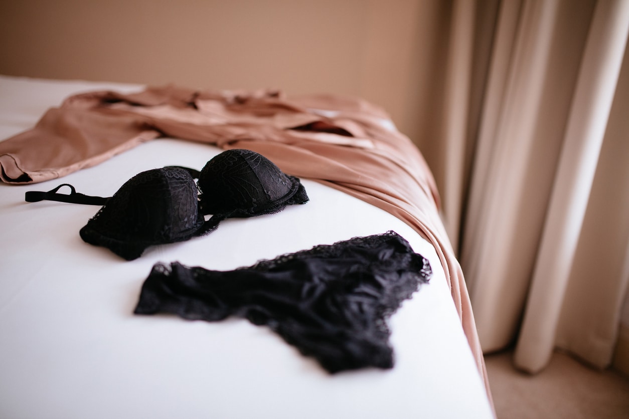 Black lace lingerie and silk robe placed in display on white sheeted bed