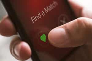 Online dating app on smart phone screen, close up. Hand touching like button with heart shape.