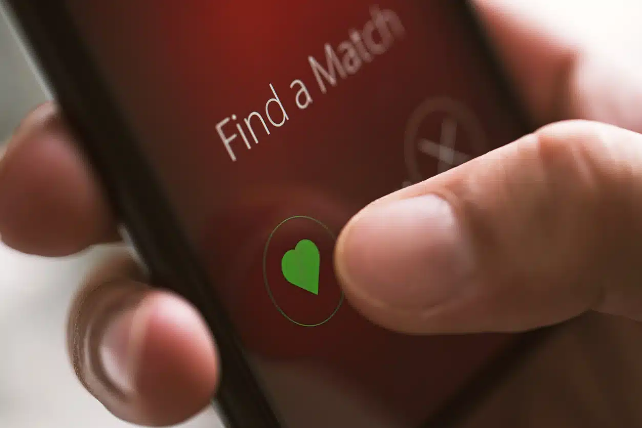 Online dating app on smart phone screen, close up. Hand touching like button with heart shape.