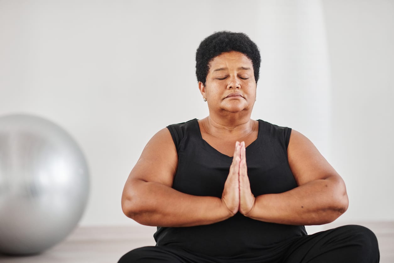 Portrait of African mature plump woman sitting in lotus position with her eyes closed and meditating during yoga