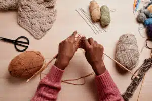 Top view of female hands knitting against wooden table in cozy light, copy space
