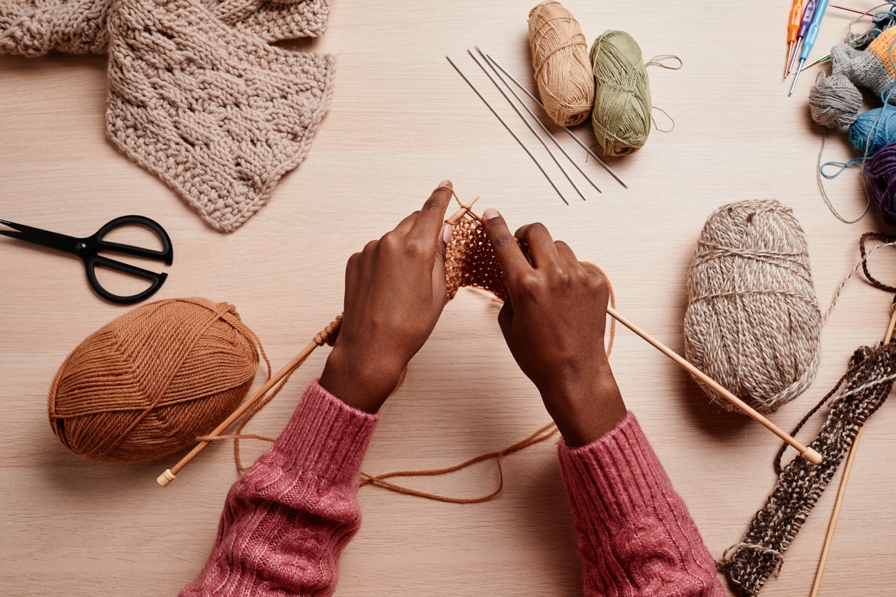 Top view of female hands knitting against wooden table in cozy light, copy space