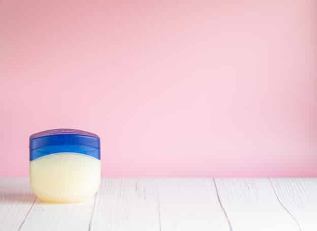 Vaseline or petroleum jelly in a clear jar on wooden surface with pink wall background with copy space for text. Skin care ointment
