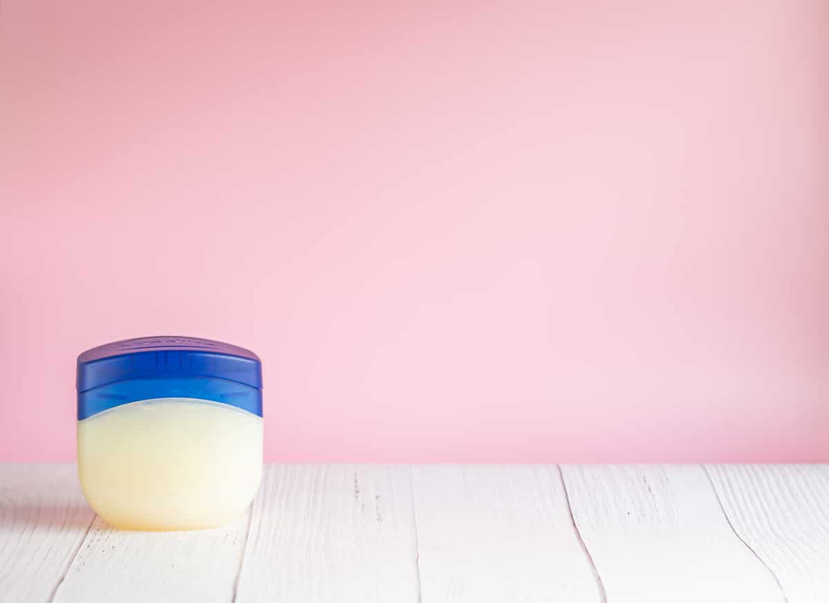 Vaseline or petroleum jelly in a clear jar on wooden surface with pink wall background with copy space for text. Skin care ointment