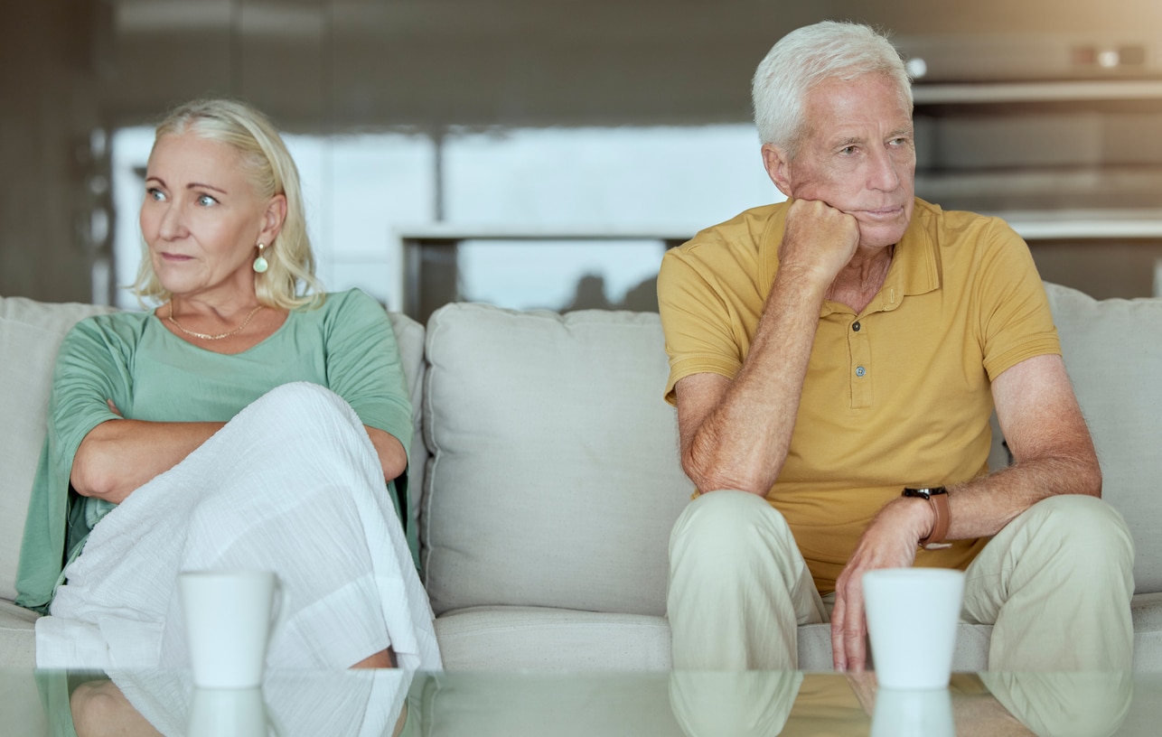 Unhappy elderly couple sitting on a sofa together after arguing. Senior caucasian man and woman looking stressed and ready for divorce
