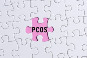 PCOS text on white jigsaw puzzle over pink background. Polycystic Ovary Syndrome Health Care concept.