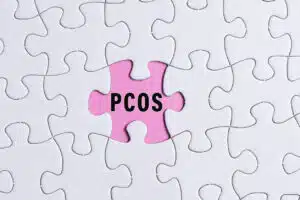 PCOS text on white jigsaw puzzle over pink background. Polycystic Ovary Syndrome Health Care concept.