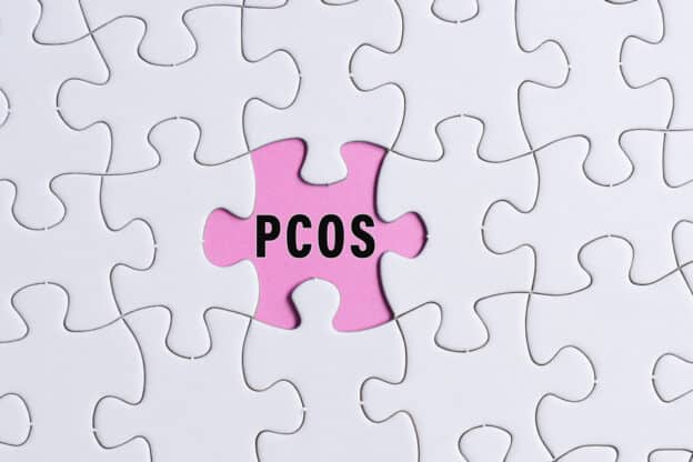 PCOS text on white jigsaw puzzle over pink background. Polycystic Ovary Syndrome Health Care concept.