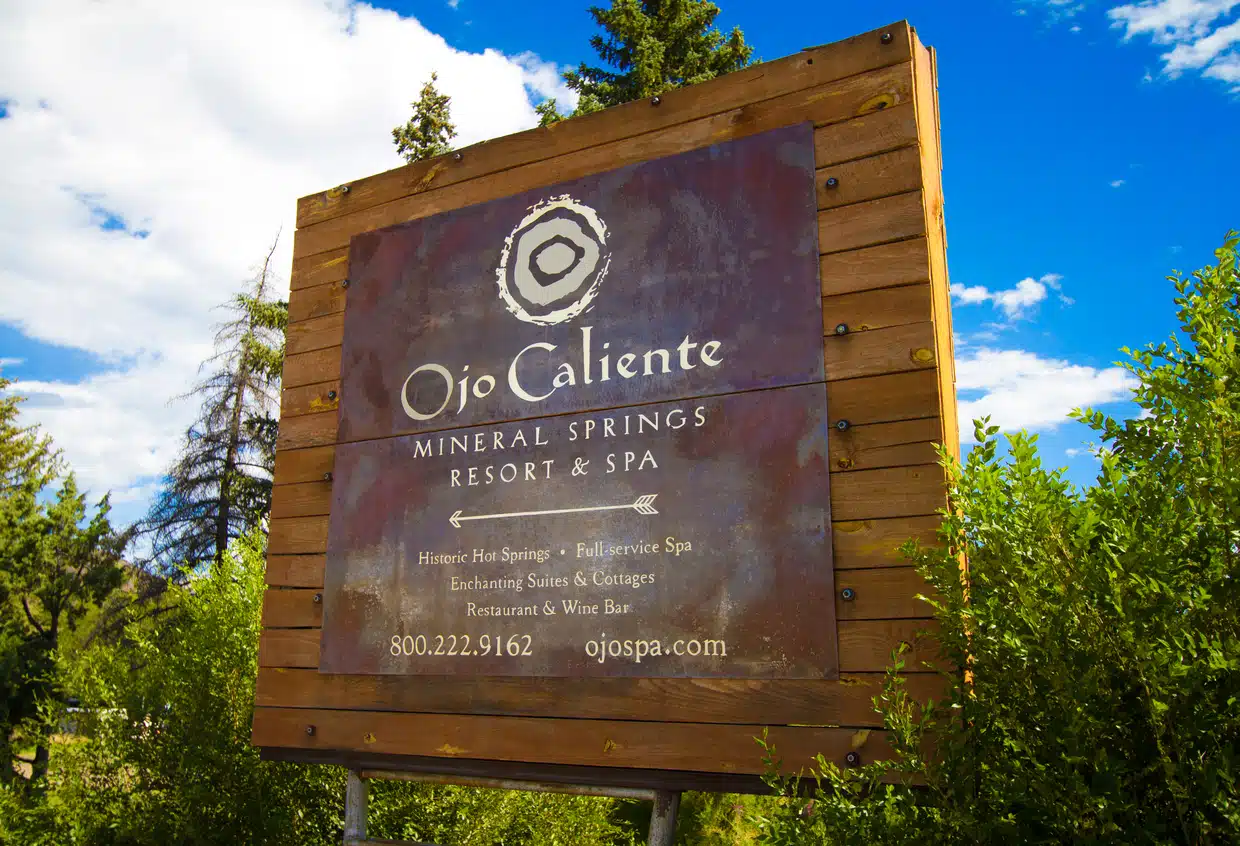Ojo Caliente, NM, USA - August 19, 2016: A large wooden sign pointing to the historic Ojo Caliente mineral springs spa, 50 miles north of Santa Fe.