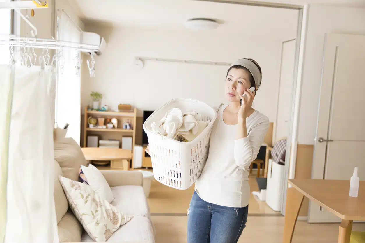busy woman holding laundry in living room answering phone