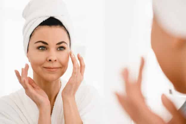 woman putting on face cream after the shower; beauty pie feature