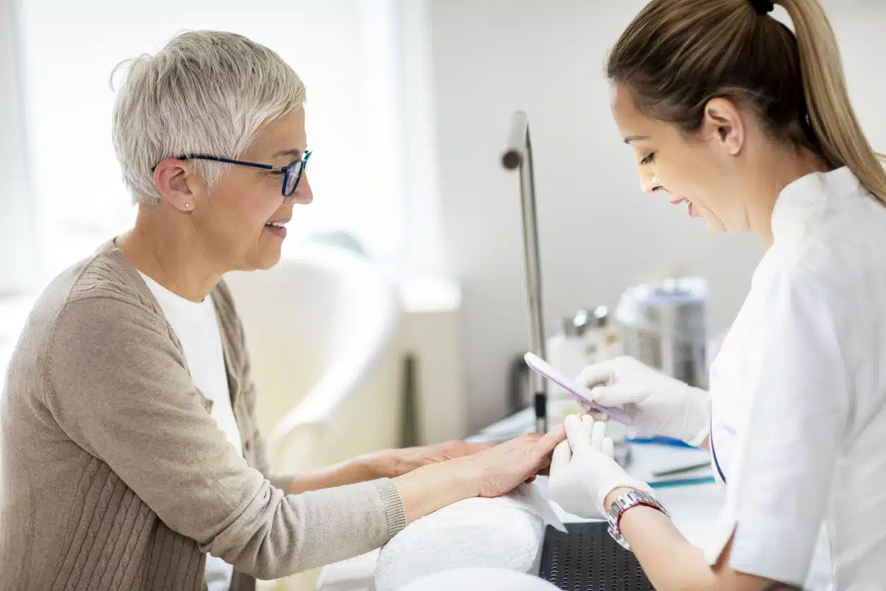 Manicure specialist tidying up an elderly woman's fingernails using a file in a manicure center
