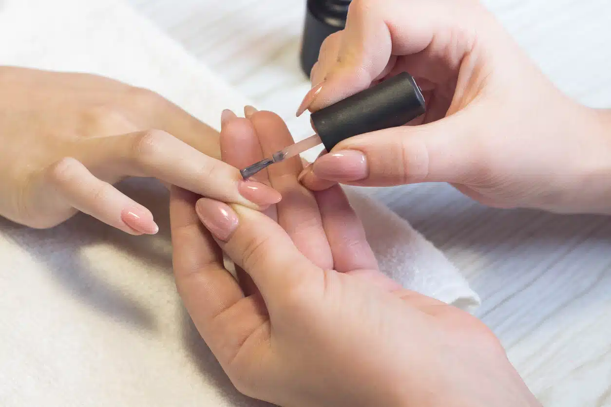 Manicure specialist applying nail polish on healthy natural female nails in beauty salon
