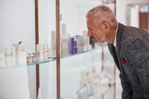 Serious elderly citizen choosing cosmetic products from a shelf at a well-lit shop