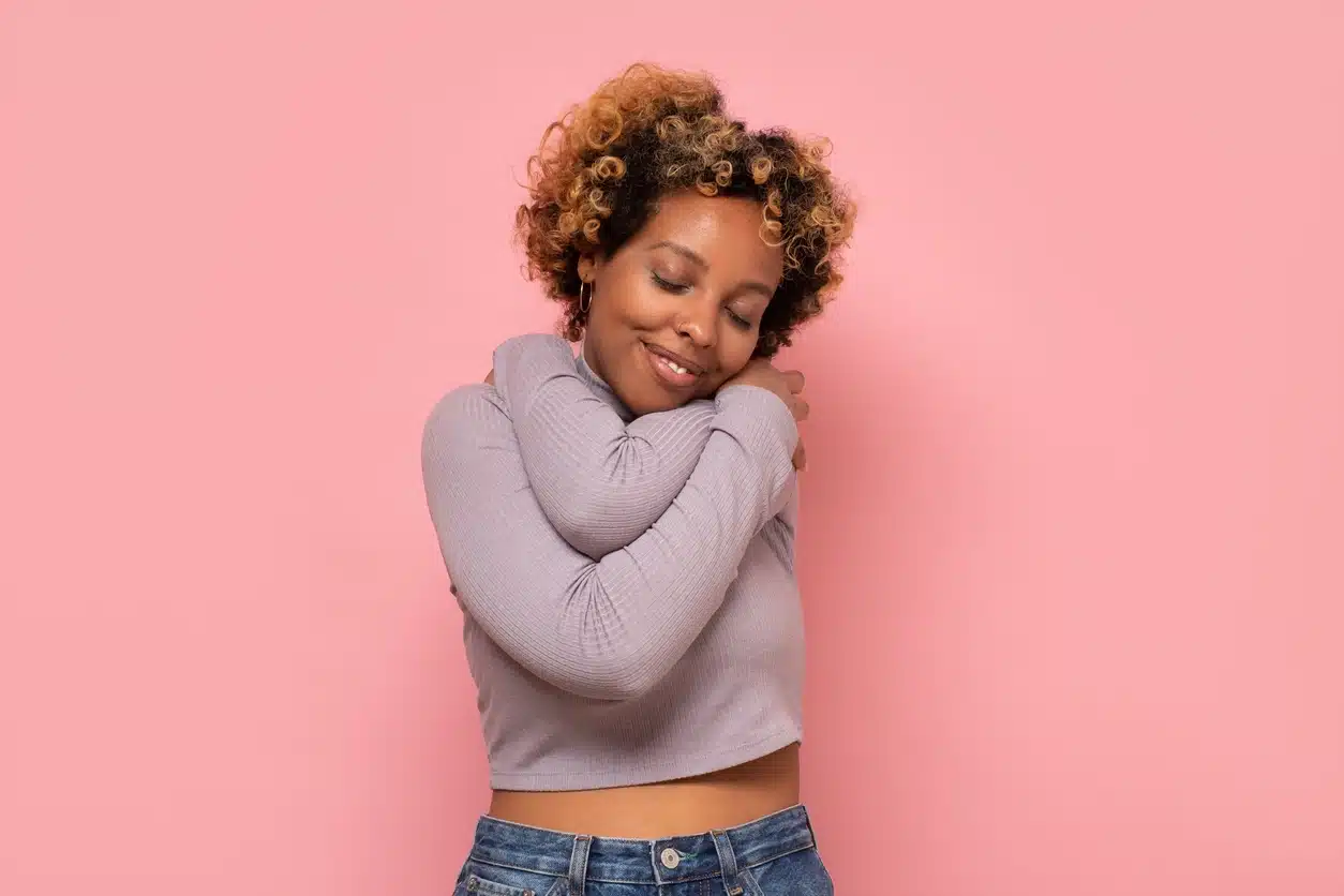 African american woman hugging herself being happy and positive, smiling confident