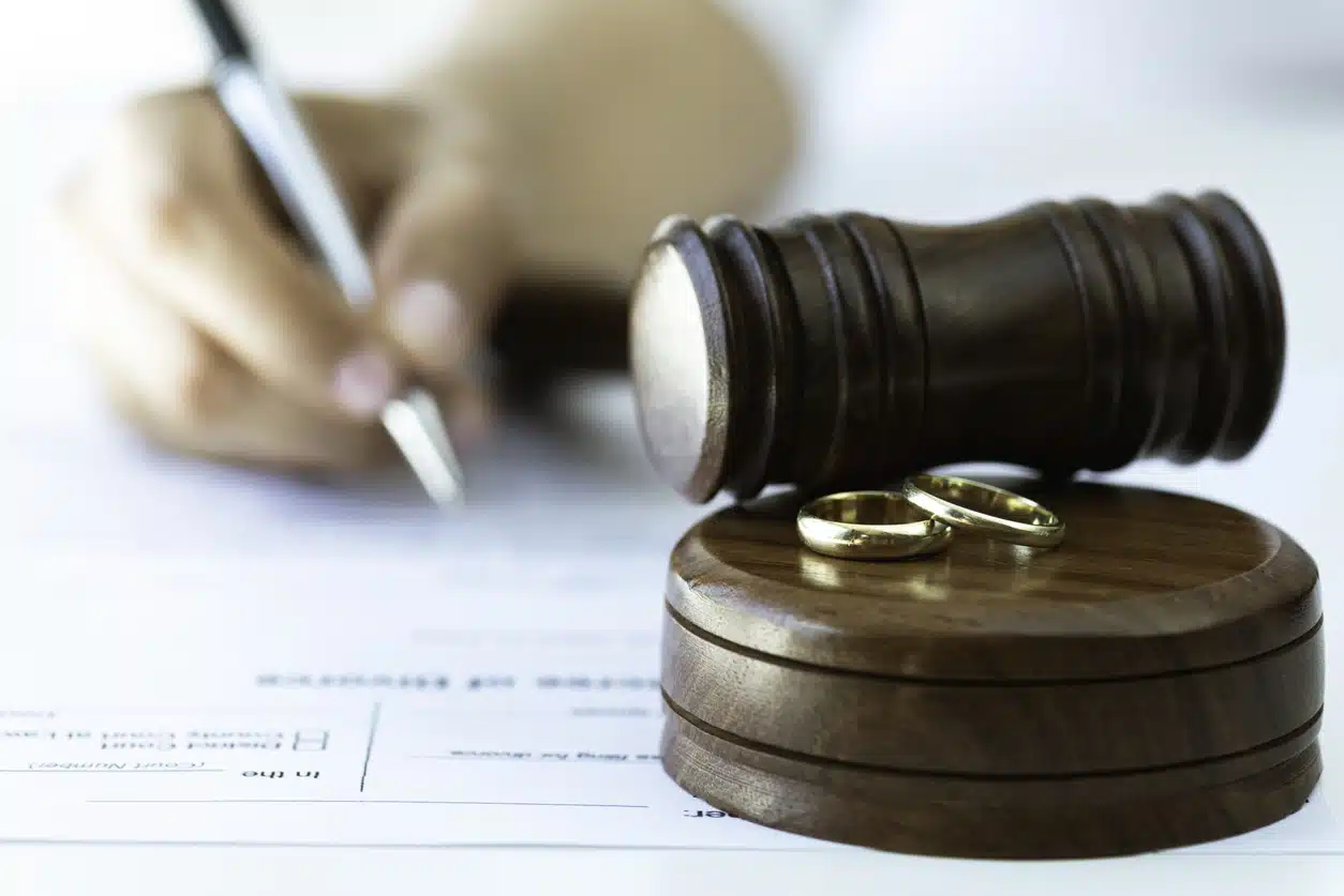 Weeding rings and gavel with a person signing a contract in the background. Representing justice steps of divorce process.