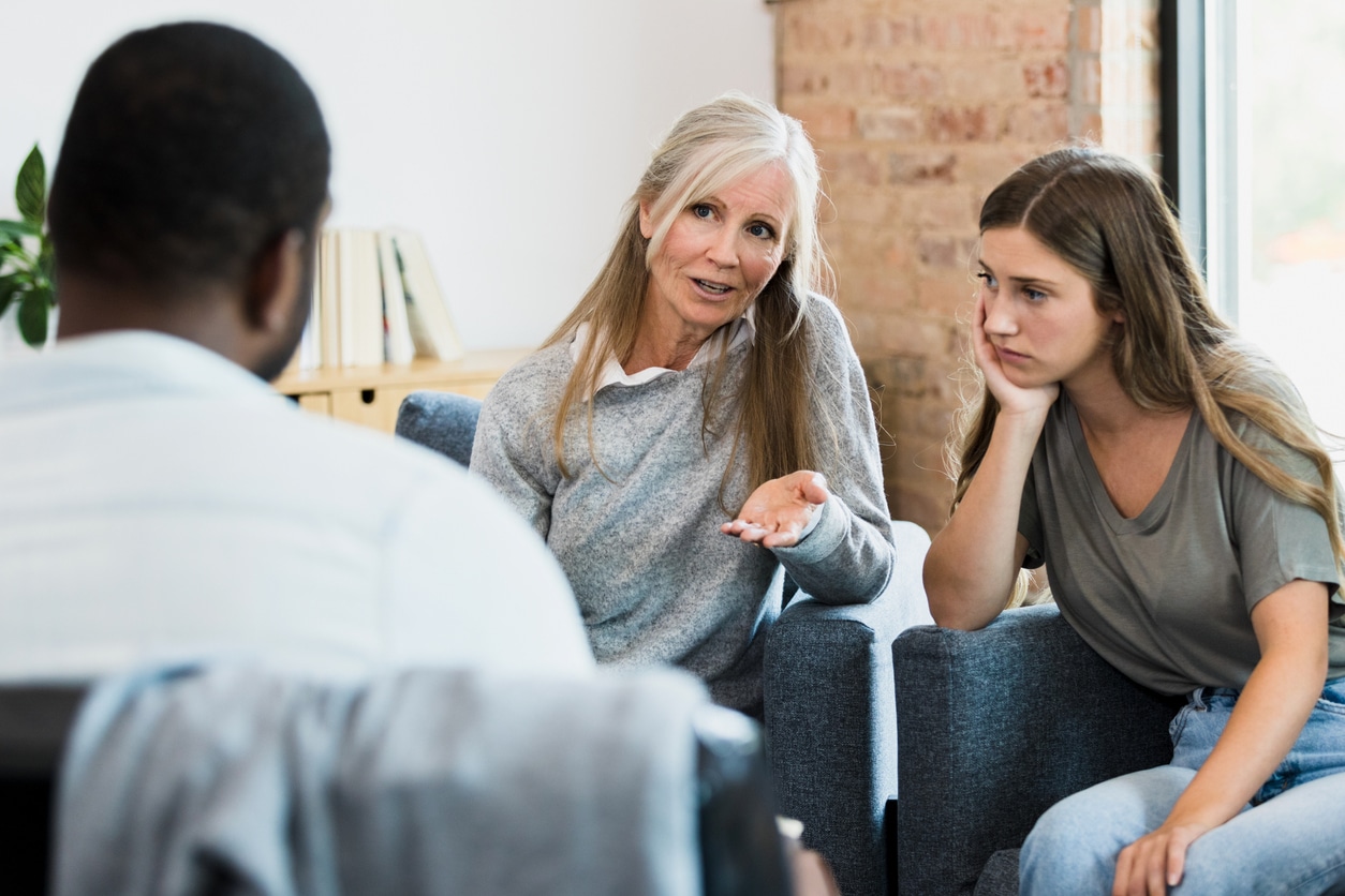 Young woman looks hopeless as mom speaks to counselor