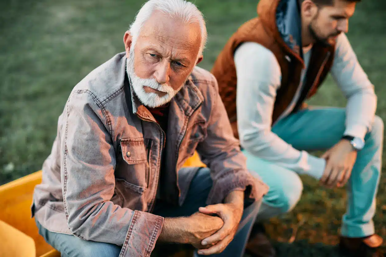 Displeased senior man ignoring his son after an argument in nature.