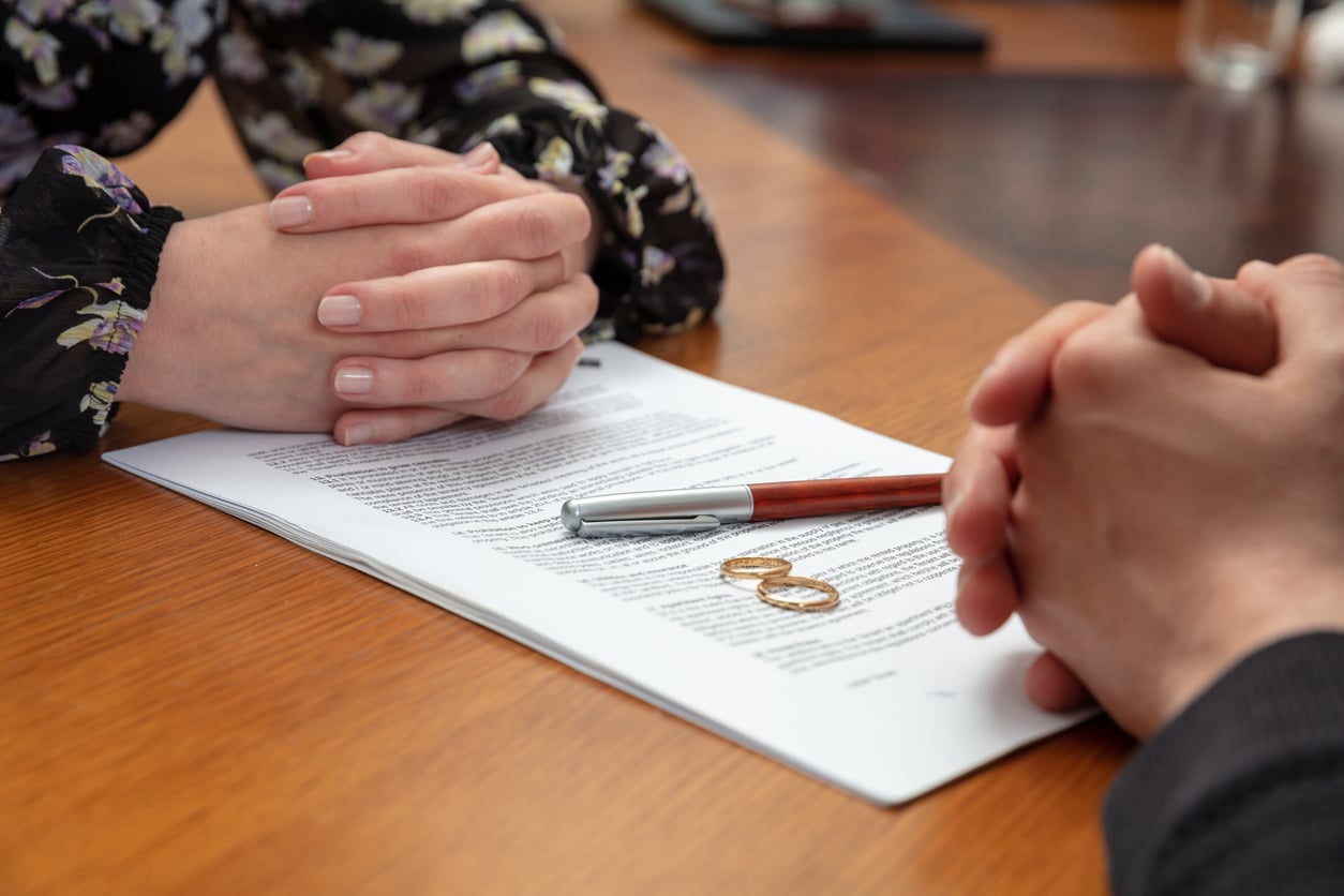 Signing a divorce, marriage dissolution documents and agreement. Wife and husband hands, wedding rings and legal papers for signature on a wooden table, lawyer office