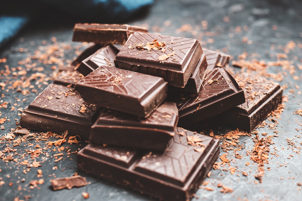Dark chocolate bar pieces on dark background with grated chocolate, pile chunks of broken chocolate.