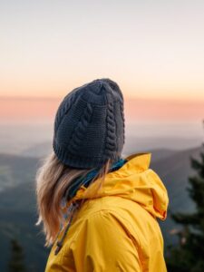 Woman with knit hat and yellow jacket looking at mountain range during sunset. Relaxation during hiking in mountains