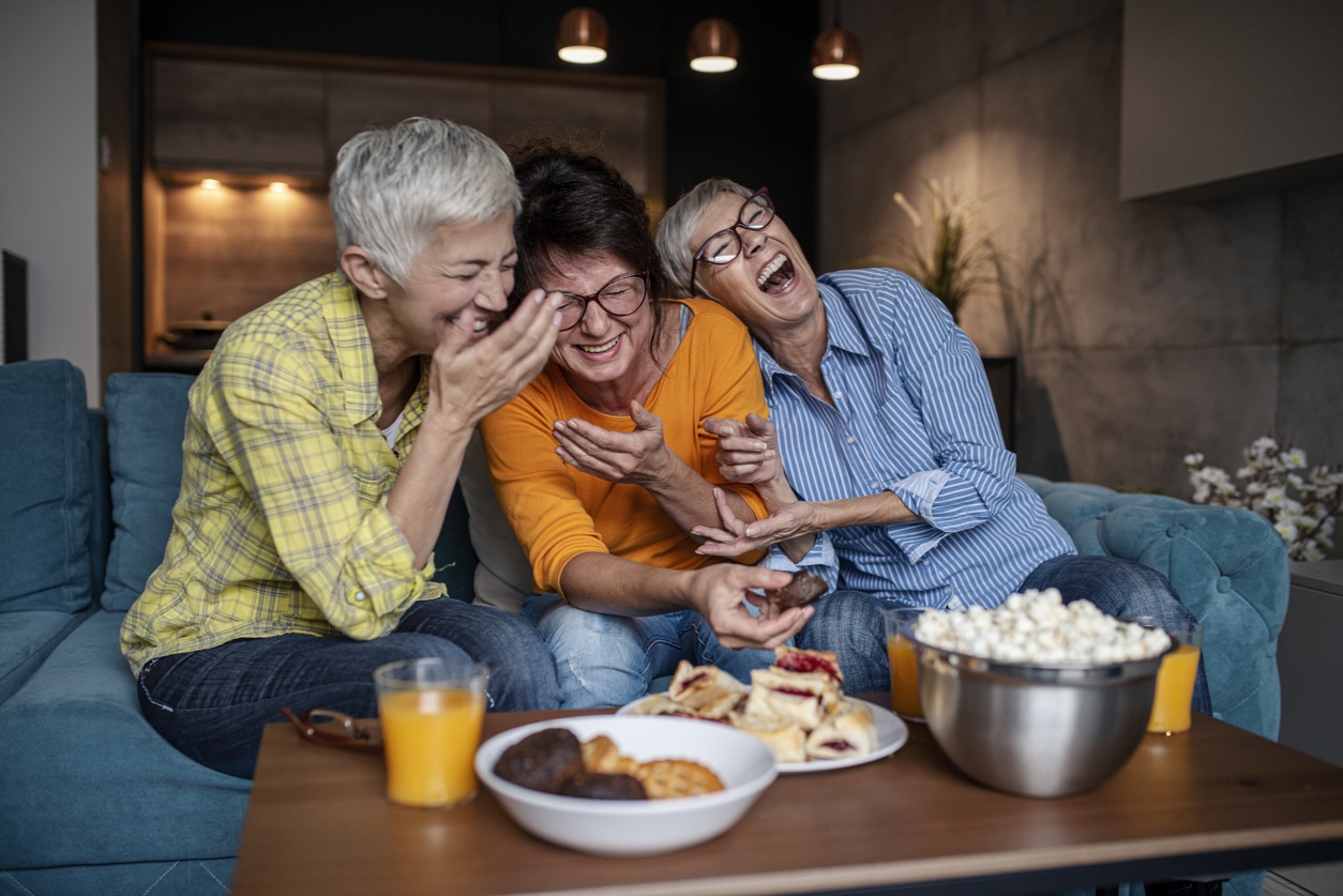 Three senior women having wonderfull time while eating sweet and salty snacks in the living room