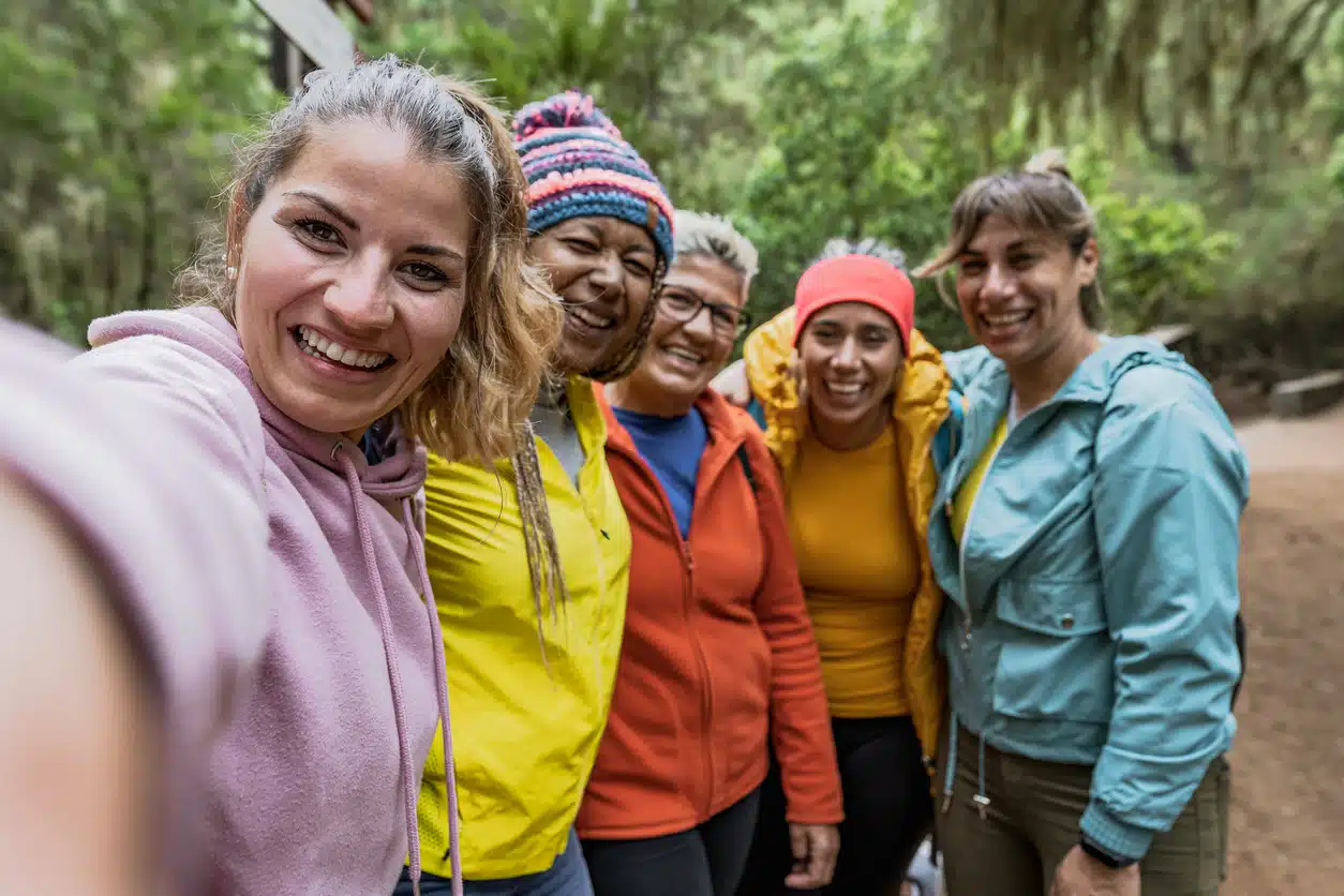 Group of women with different ages and ethnicities having fun taking selfie while walking in foggy forest - Adventure and travel people concept