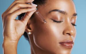 Studio shot of a young woman applying an oil to her face against a blue background