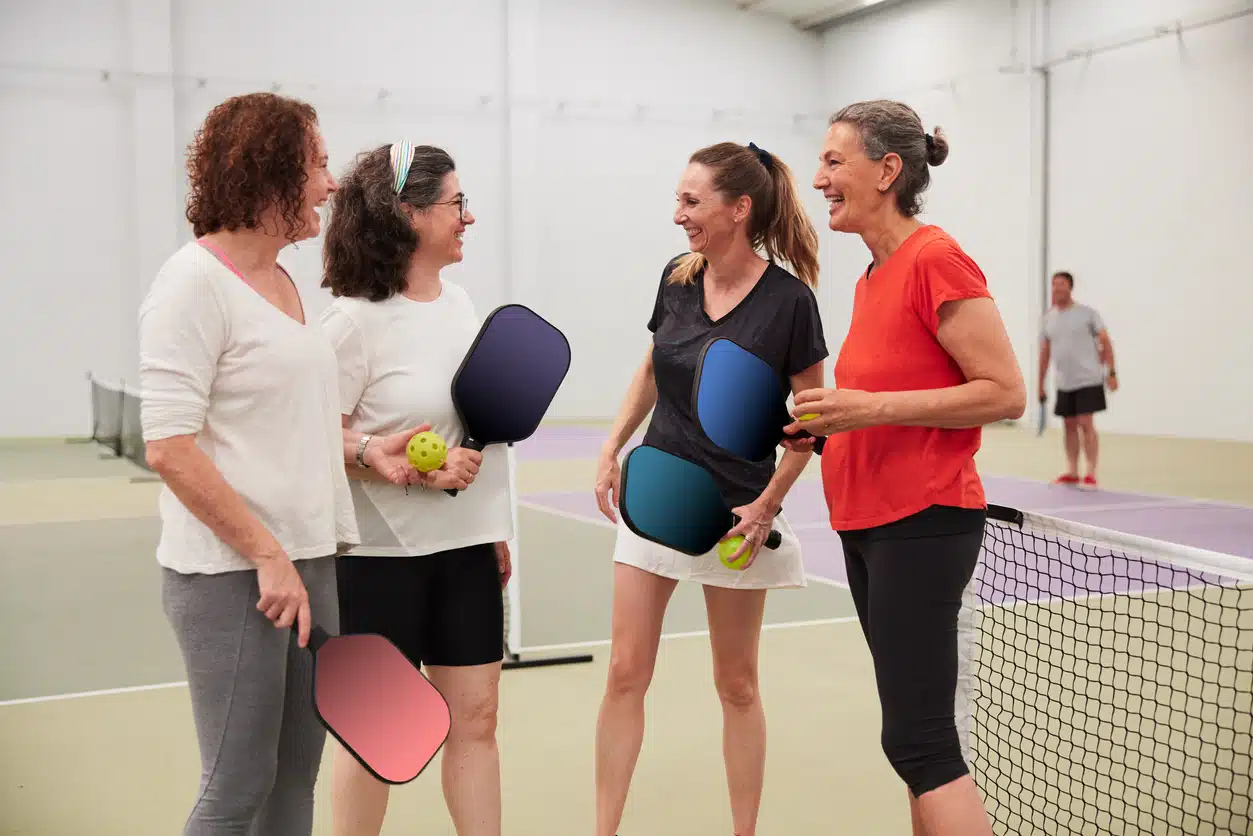 Four middle-aged women stand next to the net in sports attire.