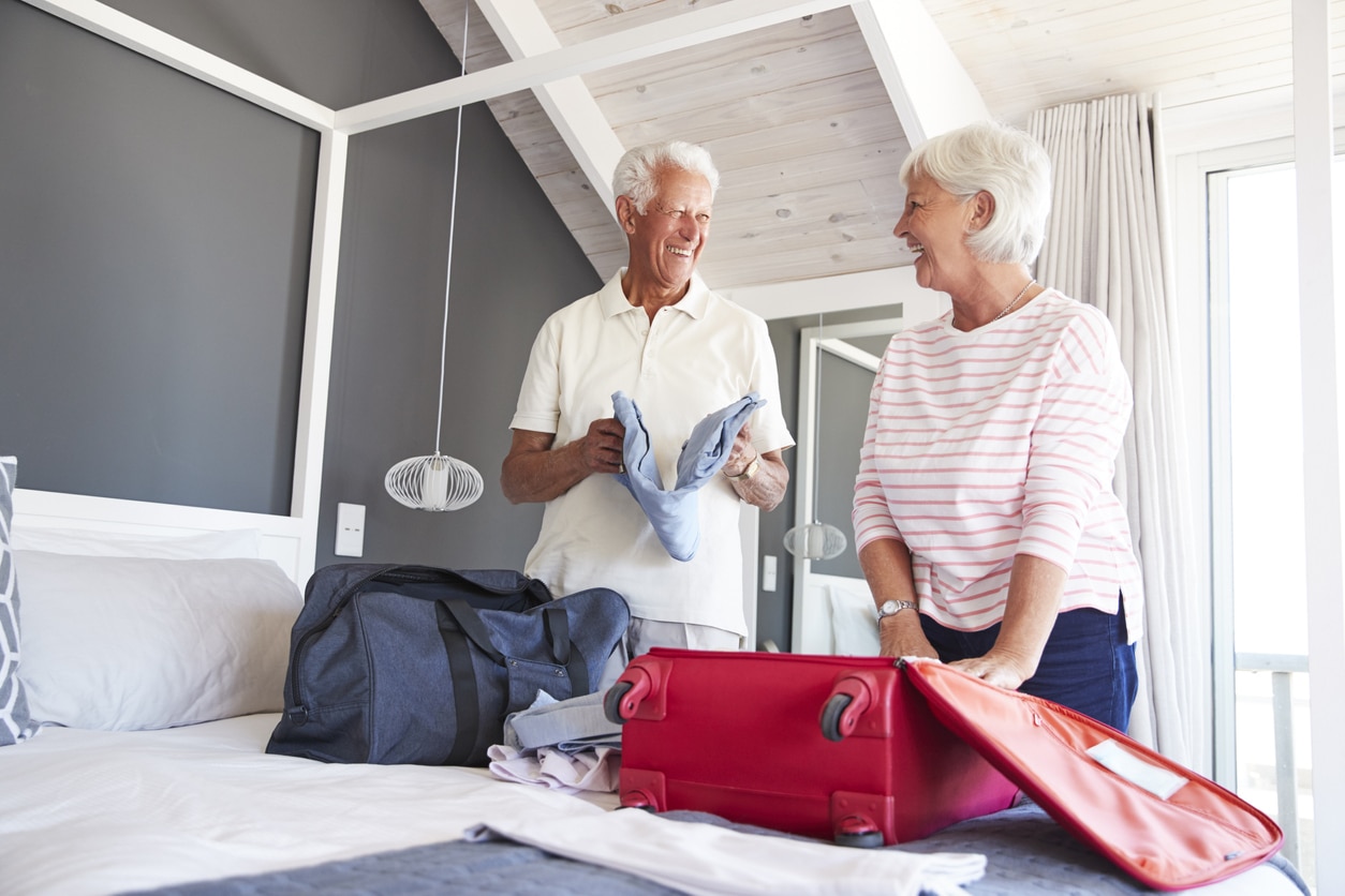 Senior Couple In Bedroom Packing Suitcase For Vacation