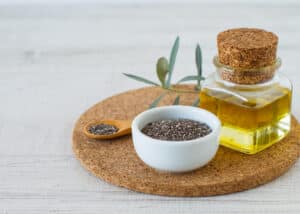 Chia oil with seeds on white wooden table background.