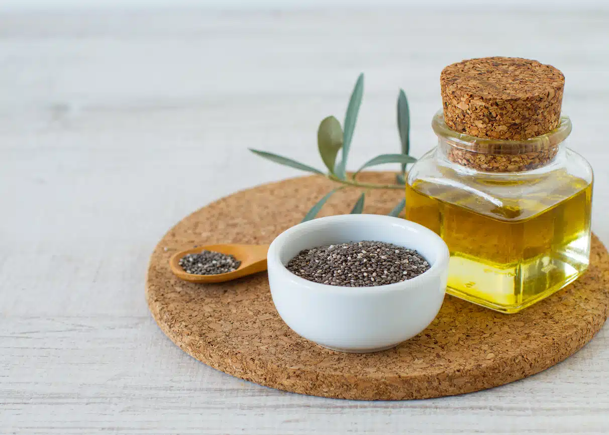 Chia oil with seeds on white wooden table background.