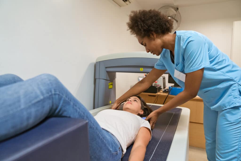 Female nurse preparing woman for bone density scan. Healthcare worker is looking at young patient lying on examination table. They are at hospital.